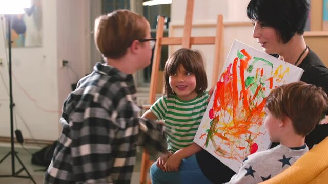Abstract art painting in woman hands has color, lines and shapes, but it are not intended to represent objects or living things. The boy artist tries to explain the idea that he presents in his work.