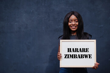 African woman hold white board with Harare Zimbabwe inscription. Most populous city in Africa concept.