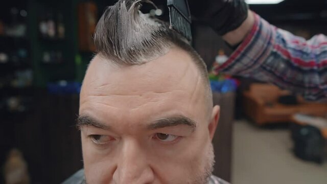 Barber dyes bearded man's mohawk with hair dye.