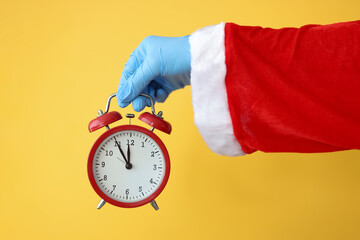 Santa clauss hand in rubber glove holding red alarm clock closeup