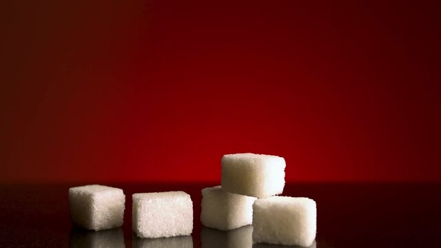 Light shines on stack of sugar cubes that lying on dark table surface isolated on red background. Stock footage. Close up of white sugar, concept of food and cooking. 