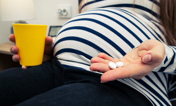 The pills in the pregnant woman's hand sitting on the bed