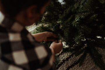 Woman in plaid shirt sitting on room floor and decorate Christmas tree. Earthy colors.