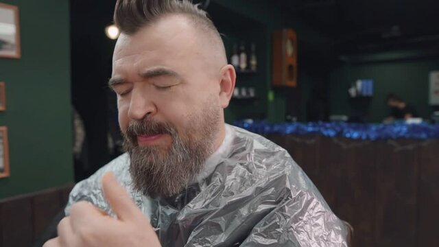 A man removes hair from his mouth while sitting on a haircut