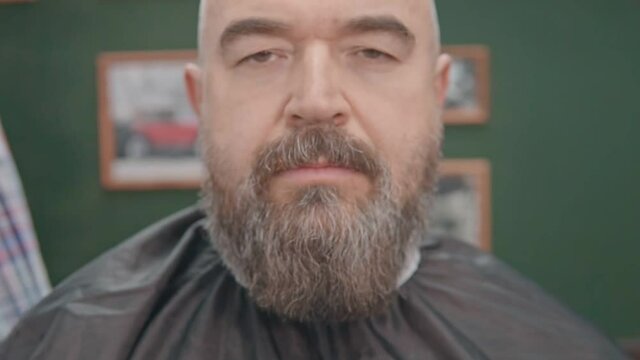 A serious man with a gray beard in a hairdressing peignoir
