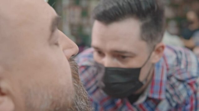 A hairdresser in a mask cuts a man's beard. Close-up.