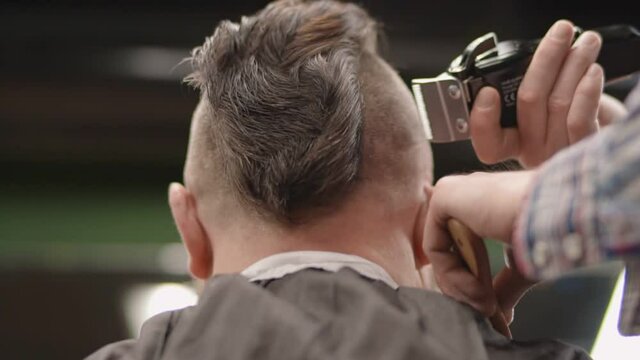 Hairdresser shaves the temple of a man with a trimmer.