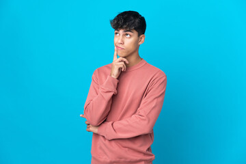 Fototapeta premium Young man over isolated blue background having doubts and thinking