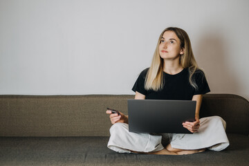 Impulse Buying, Online Shopping, fast fashion, shopaholic, spending money concept. Young woman at home holding credit card and using laptop computer and cell phone