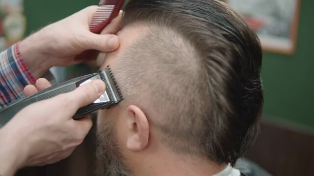 Hairdresser shaves the temple of a man with a trimmer