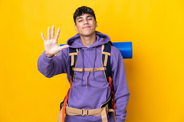 Young mountaineer man with a big backpack over isolated yellow background counting five with fingers