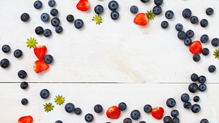 Fresh fruit in a symmetrical arrangement with copy space in the middle from directly above. Flat lay composition with red strawberries with green leaves and blue huckleberries at on a kitchen table.