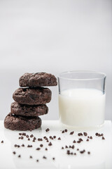 Stack of round chocolate chip cookies and glass of milk on reflective surface over white background