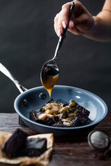 Close up of a hand with spoon pouring melted caramel over fresh hot brownies in pan on top of wooden kitchen table