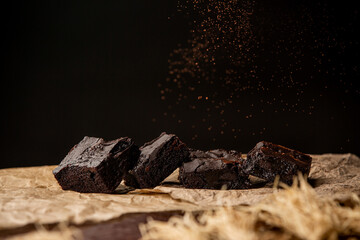 Delicious chocolate brownies on baking parchment paper sprinkled with cocoa powder over black background