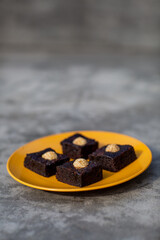 Brownies decorated with sesame balls on on yellow plate on top of stone grey background
