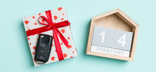 Top view of car key on a gift box with red hearts and festive calendar on colorful background. The fourteenth of february. Present for Valentine's Day concept
