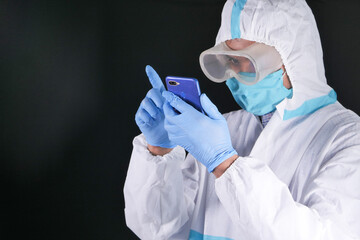 portrait of a male doctor wearing PPE using smart phone 