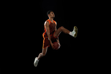 Overcome. Young purposeful african-amrican basketball player training, practicing in action, motion isolated on black background. Concept of sport, movement, energy and dynamic, healthy lifestyle.