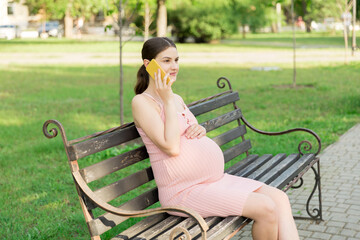 pregnant woman sits on a park bench and talking on phone