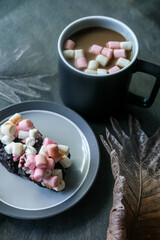 Hot chocolate or cocoa with marshmallows and rocky road brownies on a plate on top of stone grey background
