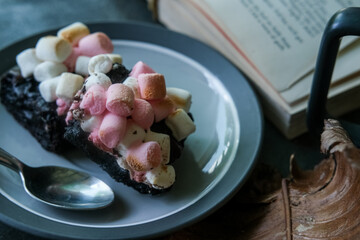 Rocky road brownies with marshmallows on a plate and a book on top of stone grey background