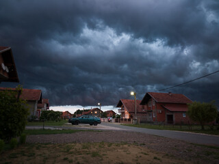 Stormy severe weather during storm with dark scary clouds, above settlement during summer evening.