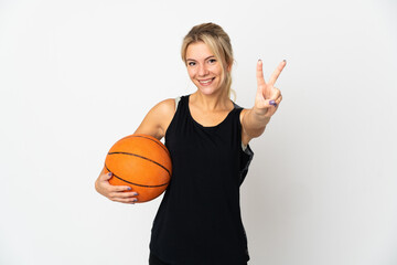 Young Russian woman playing basketball isolated on white background smiling and showing victory sign