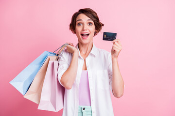 Photo of funny amazed young lady wear white shirt holding bank card colorful bargains isolated pink...