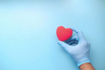  man hand in protective gloves holding red heart on blue 