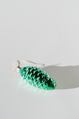 Green pine cone glass vintage christmas bauble on white background with sunlight and shadow