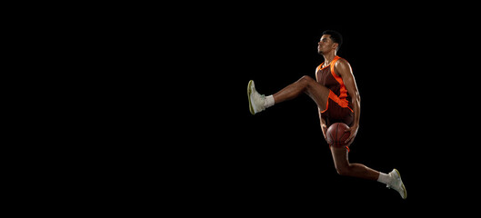 Fototapeta na wymiar Flying. Young purposeful african-amrican basketball player training, practicing in action, motion isolated on black background. Concept of sport, movement, energy and dynamic, healthy lifestyle.