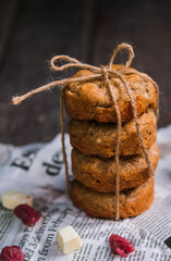 Stack of round raspberry white chocolate chip cookies tied with a rope on newspaper on top of wooden rustic background