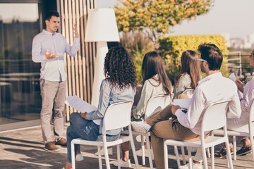 Portrait of business persons sit chairs hold papers listen to speak person explaining talking outdoors
