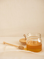 Glass jar with acacia honey and a wooden spoon for honey on a light background in the morning light