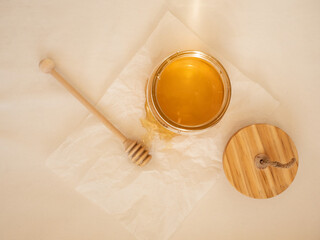 Glass jar with acacia honey and a wooden spoon for honey on a light background in the morning light