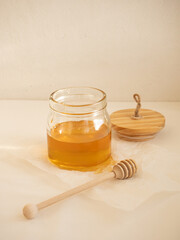 Glass jar with acacia honey and a wooden spoon for honey on a light background in the morning light
