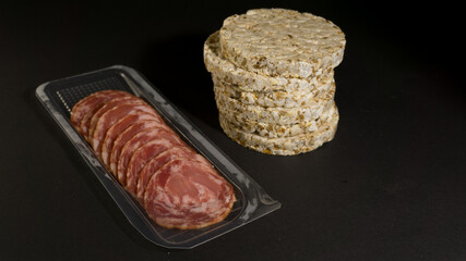 Grain crispbreads crispy rice and diet bread with smoked sausage. Rice cake puffed rice with salami, sausage, balyk, smoked meat on black background