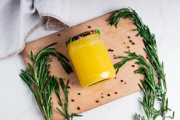 Ghee clarified butter desi in glass jar with rosemary on natural wooden background.