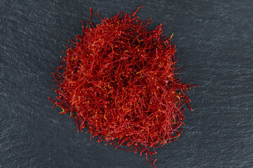 Pile of dry saffron threads on a black textured background. Spice.