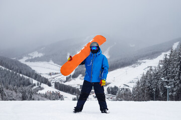 The guy hold on the shoulder orange snowboard in winter