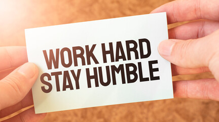 WORK HARD STAY HUMBLE word inscription on white card paper sheet in hands of a businessman. recap concept. red and white paper
