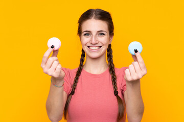 Young woman over isolated yellow background offering colorful French macarons