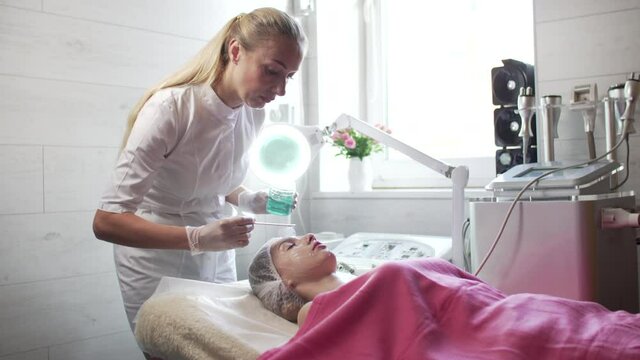 A beautician applies gel to the patient's woman's face before the RF-lifting procedure. Wide shot. Slider shot.