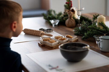 Christmas table decoration. Cookies in a herringbone-shaped plate. Festive atmosphere at home. Cooking New Year's sweets. Boy looking at sweets