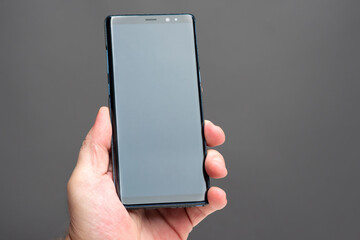 Man hand with a smartphone. A man holds a mobile phone vertically. A smartphone with a blank screen on a gray background. A touch-screen phone next to the text space.