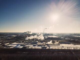 Factories, pipes with smoke on a Sunny snowless winter day, photo from a drone. Photo against the sun. Concept of ecology and nature protection.