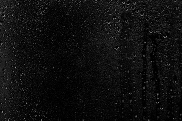 Drops of water flow down the surface of the clear glass on a black background. Texture for...