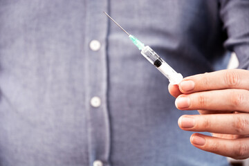 Doctor with syringe is preparing for injection, holding a plastic syringe with needle.