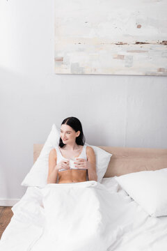 happy woman with vitiligo holding cup of coffee while resting in bed